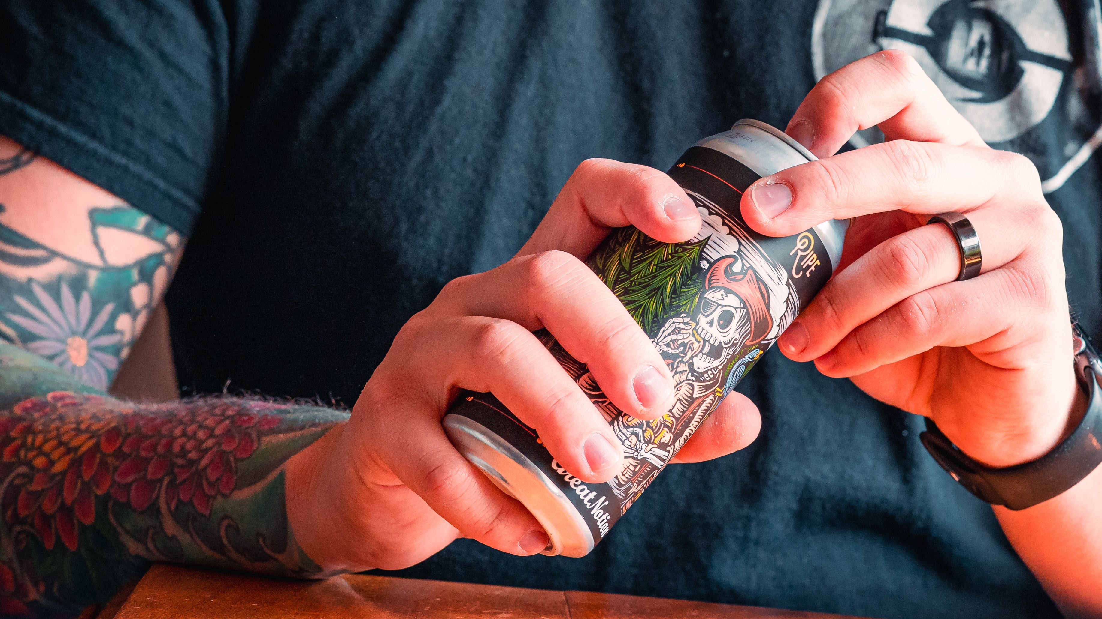 Someone cracks open a can of beer with a picture of a skeleton pirate on the label.